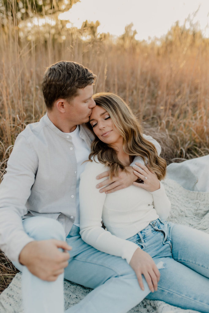 Man kissing girl's head on picnic blanket in fall engagement photo session